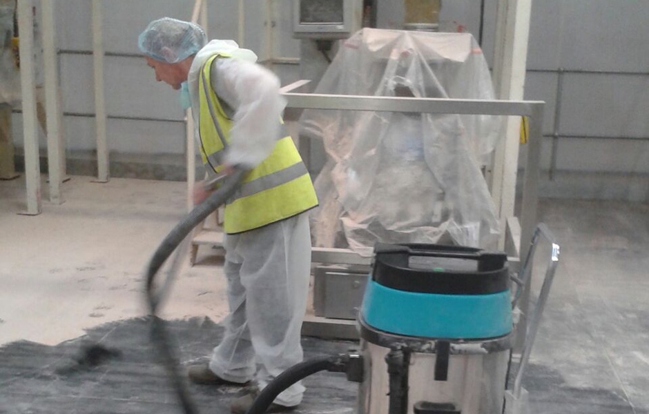 Cleaning operative using industrial vacuum on warehouse floor